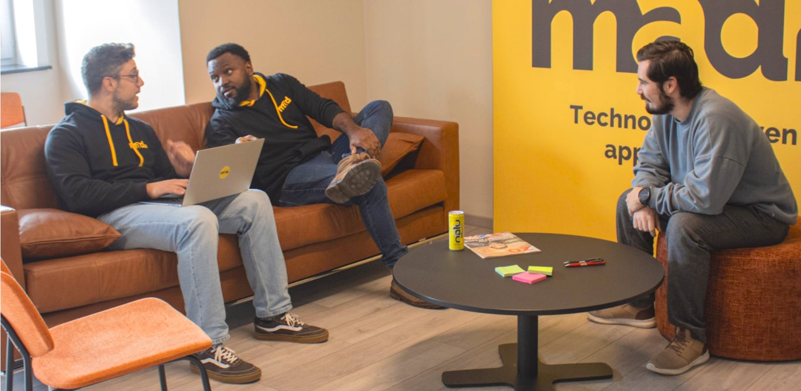 Drie IT-professionals in overleg in een creatieve kantoorruimte van mad.IT, met laptops, notities en een ontspannen sfeer tijdens een brainstormsessie over softwareonderhoud en digitale oplossingen.